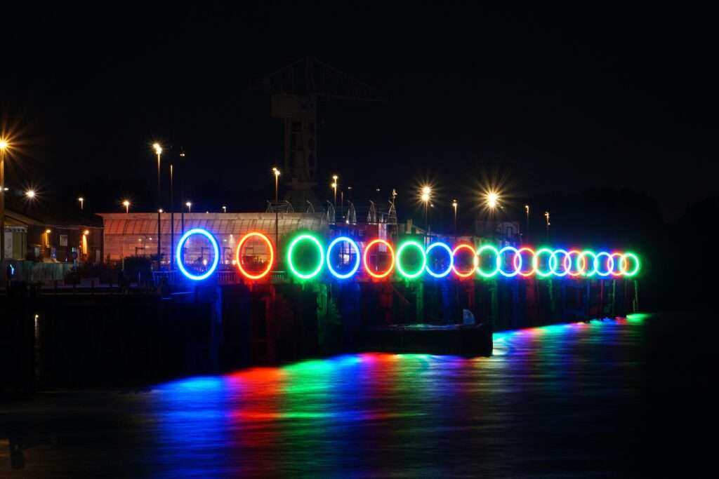 Nighttime picture of the art installation les Anneaux de Buren in Nantes, at the old docks, with reflection of the installations lighting in the water of the Loire.